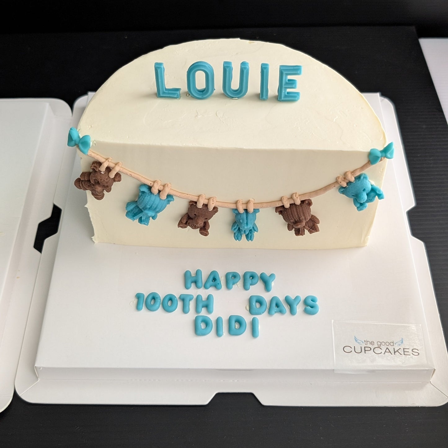 100-day baby celebration cake with cream buttercream, hand-piped teddy bear bunting in teal and brown, custom name topper, low-sugar Singapore