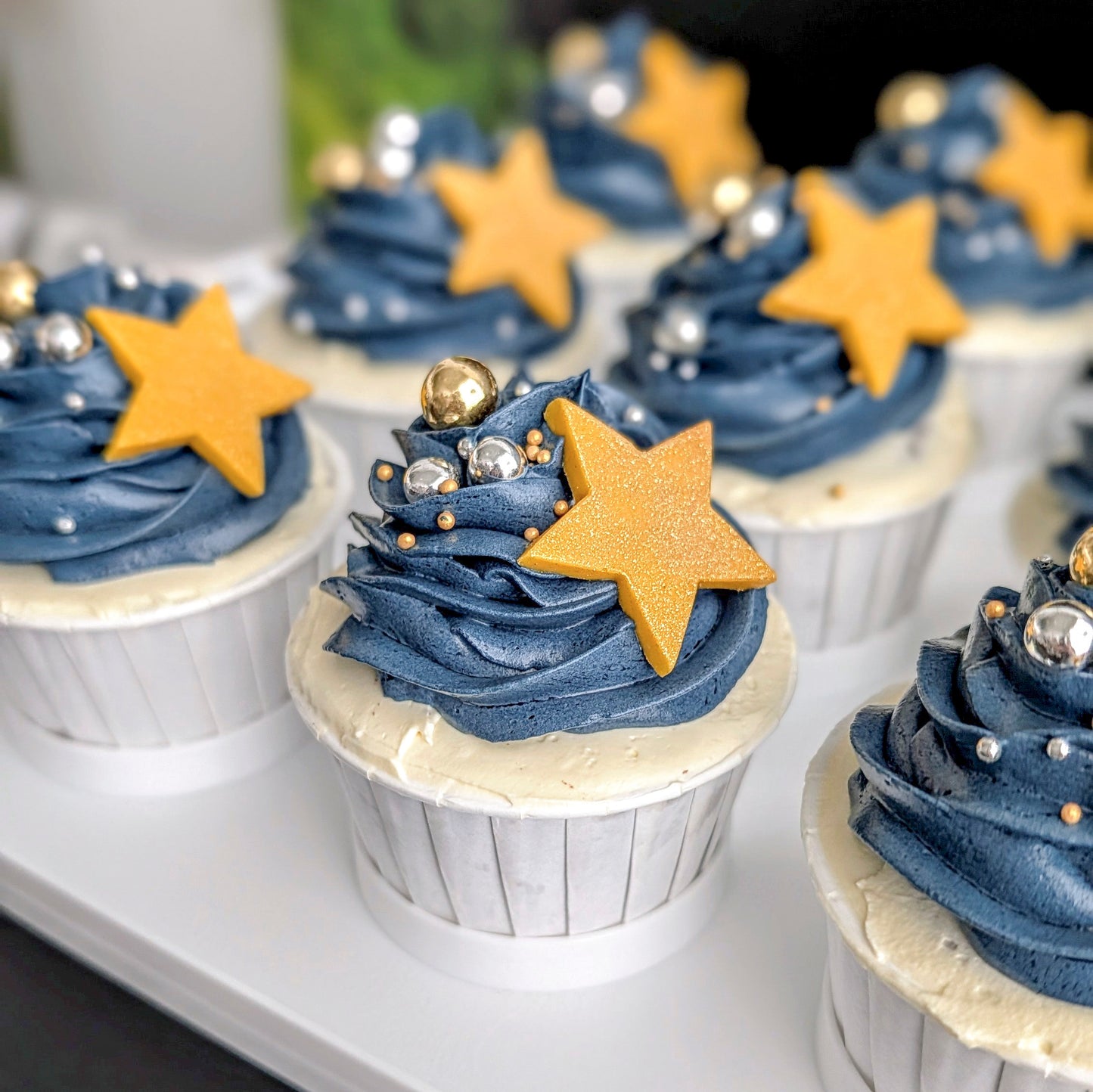 Cupcakes on a white tray— galaxy navy blue buttercream swirls topped with a gold and silver dragees and a chocolate star