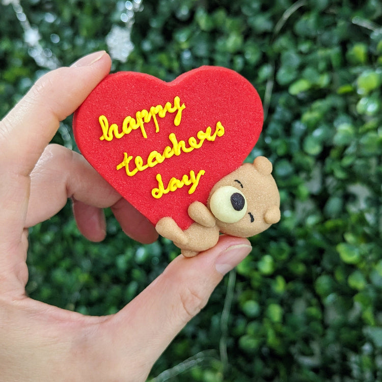 Happy Teacher's Day heart-shaped cookie with hand-piped yellow lettering and a sleepy bear, The Good Cupcakes Singapore