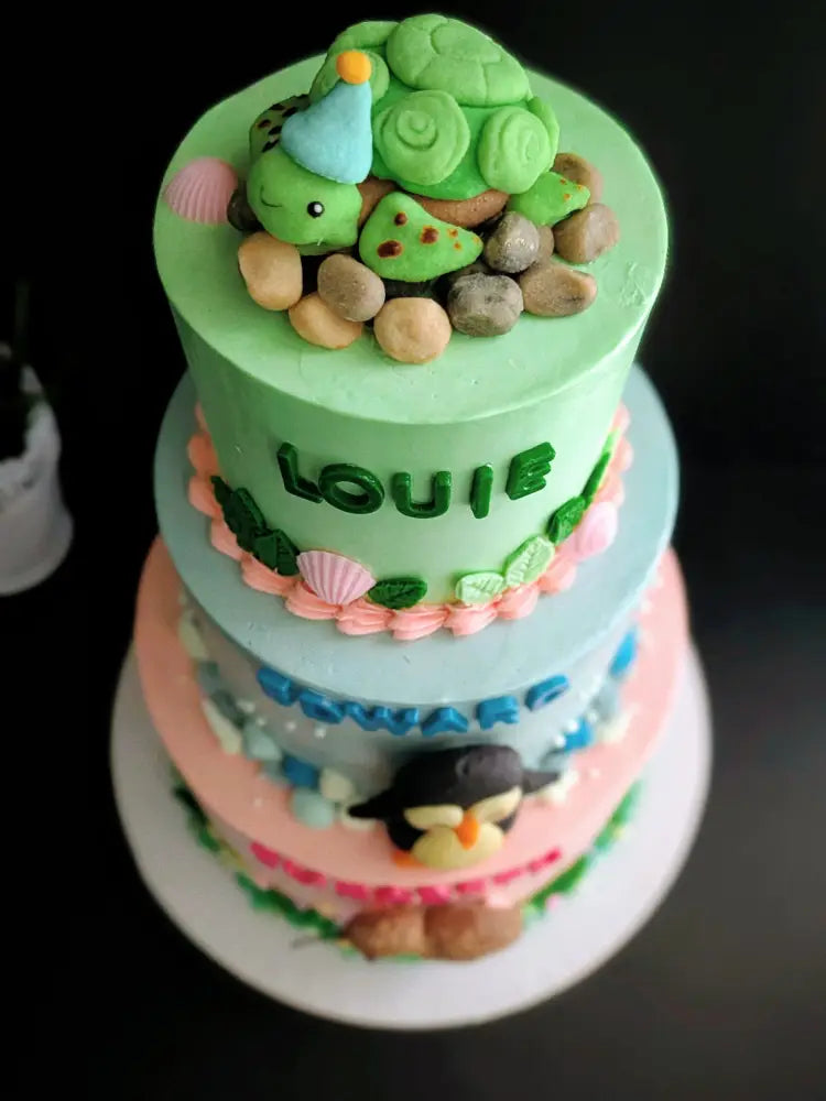 Three-tier birthday cake with turtle, penguin and kiwi bird buttercream decorations in green, blue and pink, custom name cake Singapore