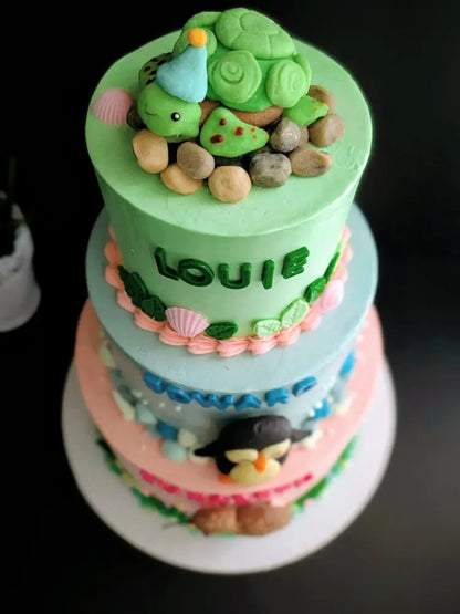 Three-tier birthday cake with turtle, penguin and kiwi bird buttercream decorations in green, blue and pink, custom name cake Singapore