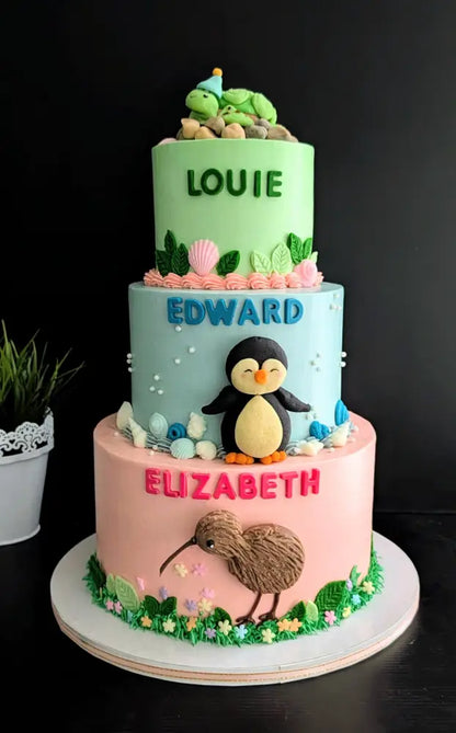 Three-tier birthday cake with turtle, penguin and kiwi bird buttercream decorations in green, blue and pink, custom name cake Singapore