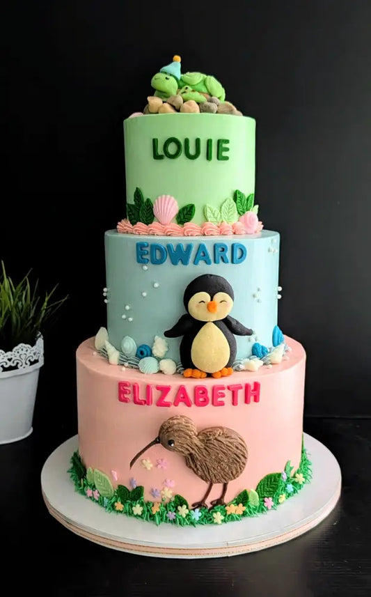 Three-tier birthday cake with turtle, penguin and kiwi bird buttercream decorations in green, blue and pink, custom name cake Singapore