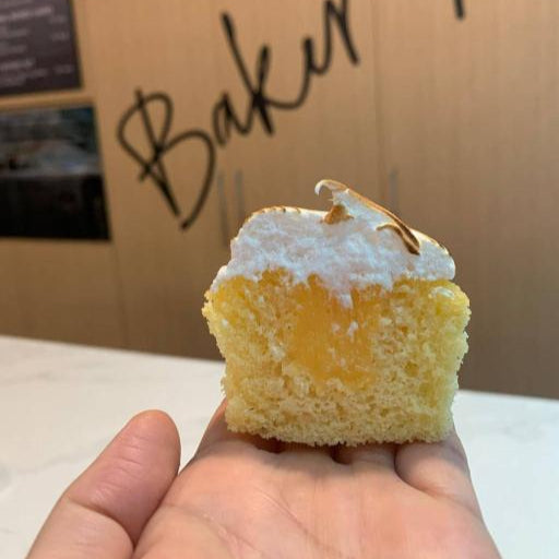 A single lemon meringue cupcake held in a person's hand, with a visible lemon curd filling and toasted meringue topping.