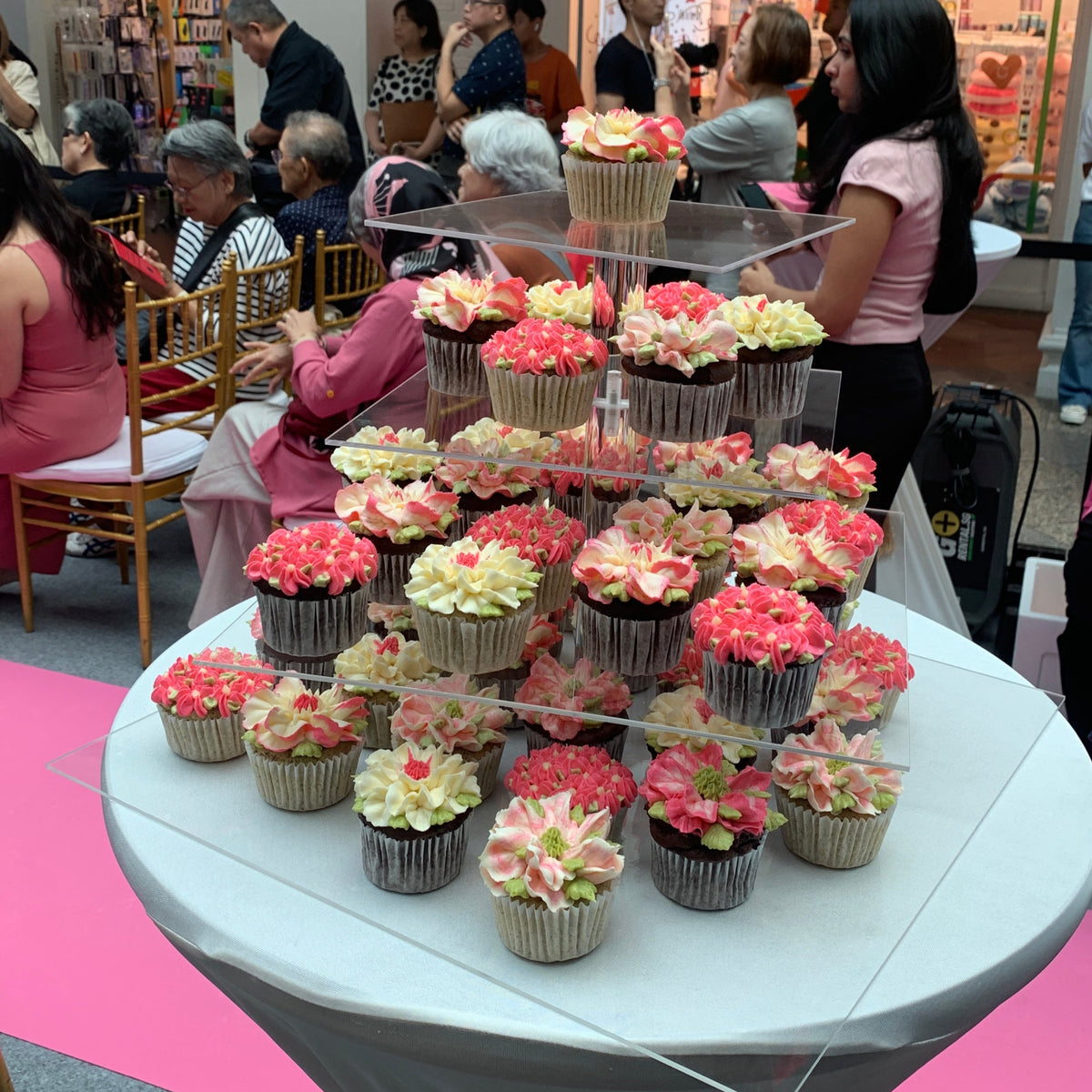 Pink, cream and green floral cupcakes arranged on a tiered acrylic display at the National Breast Cancer Awareness Month 2024 launch event.