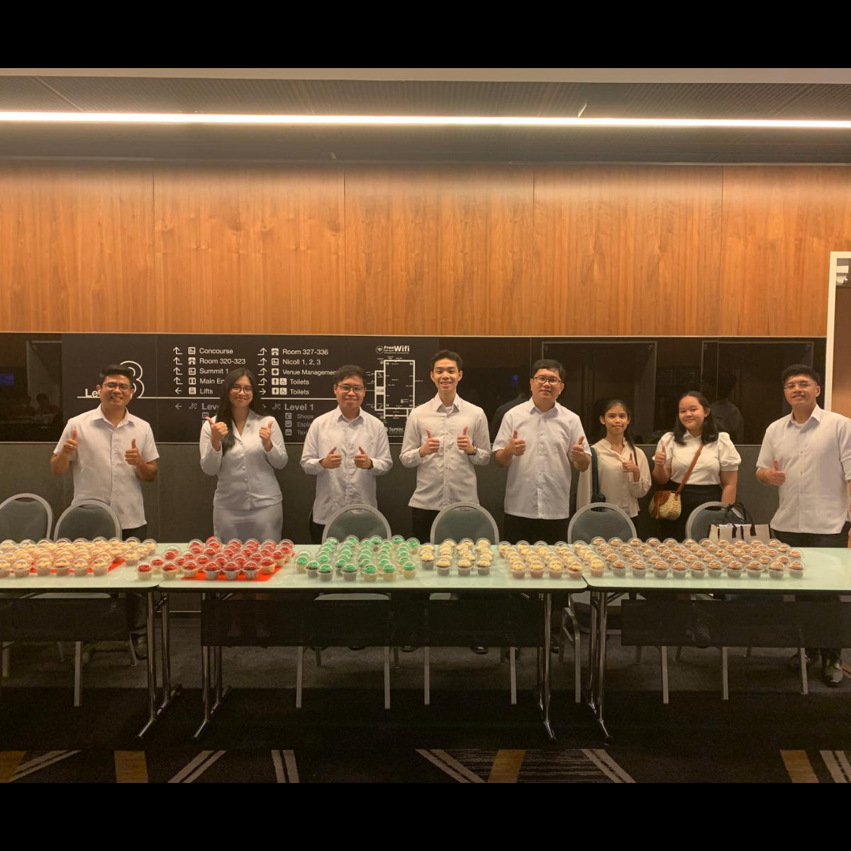 Eight event staff standing behind a long display of individually packed cupcakes in red, green and cream at Suntec Convention Centre.