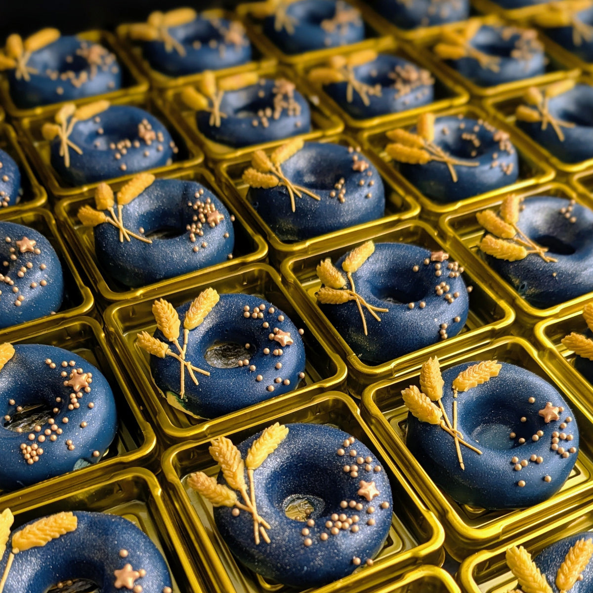 Rows of individually presented navy-blue ring cookies decorated with gold wheat sprigs, stars and metallic pearls, created for Chanel.