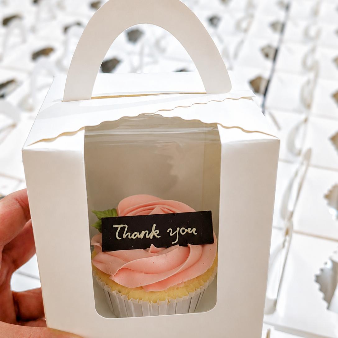 Thank you cupcake with pink rose frosting in white gift box with handle, held by hand