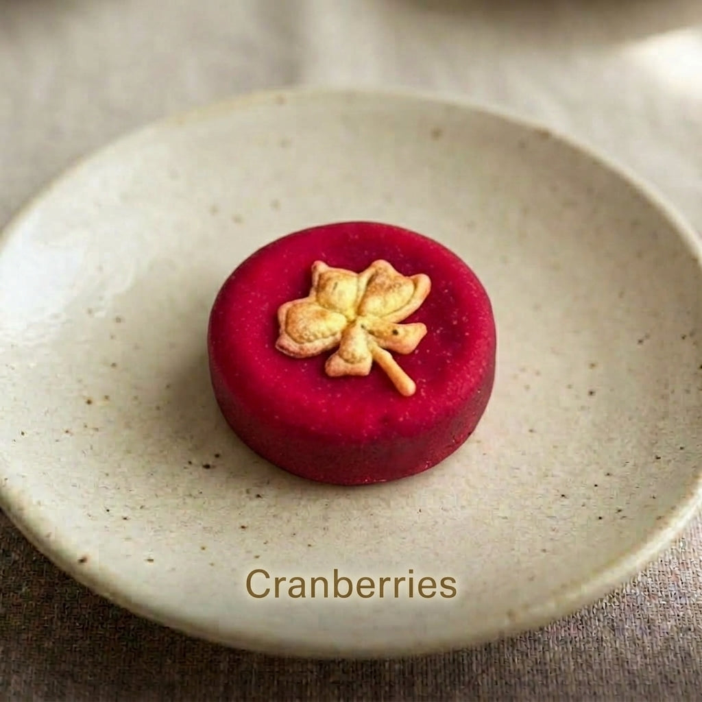 Cranberries shortbread cookie topped with a hand-piped maple leaf design, on a speckled ceramic plate.