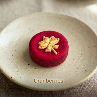 Cranberries shortbread cookie topped with a hand-piped maple leaf design, on a speckled ceramic plate.