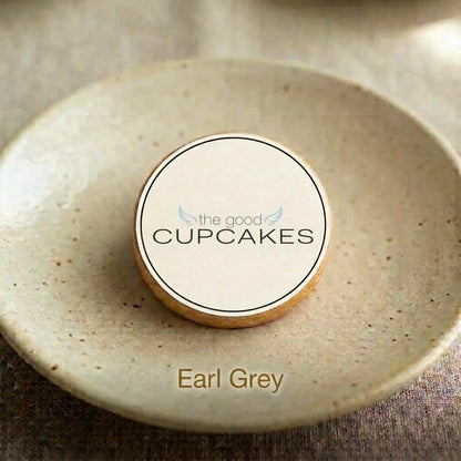 Earl Grey shortbread cookie stamped with The Good Cupcakes Company logo, on a speckled ceramic plate.