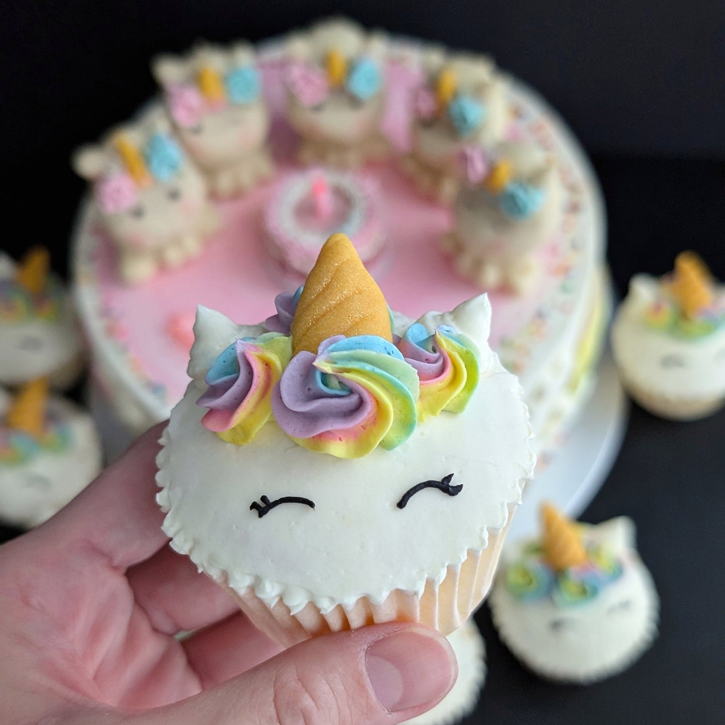 Close-up of hand holding a Rainbow Unicorn cupcake, hand-piped buttercream unicorn face and horn, custom design — The Good Cupcakes Singapore
