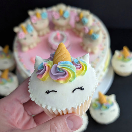 Close-up of hand holding a Rainbow Unicorn cupcake, hand-piped buttercream unicorn face and horn, custom design — The Good Cupcakes Singapore