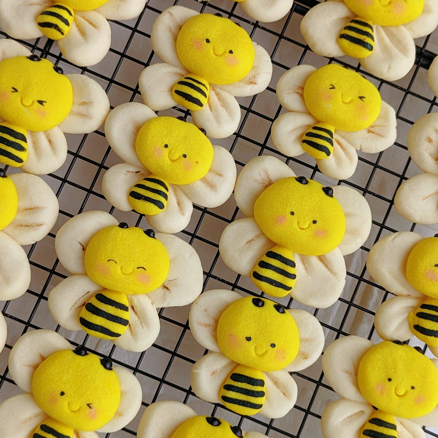 Handmade 3D bumble bee-shaped shortbread cookies on a cooling rack — yellow and black striped bee body with cream-coloured wing cookies, rosy cheeks, and a smiling face. Made to order by The Good Cupcakes, Singapore.
