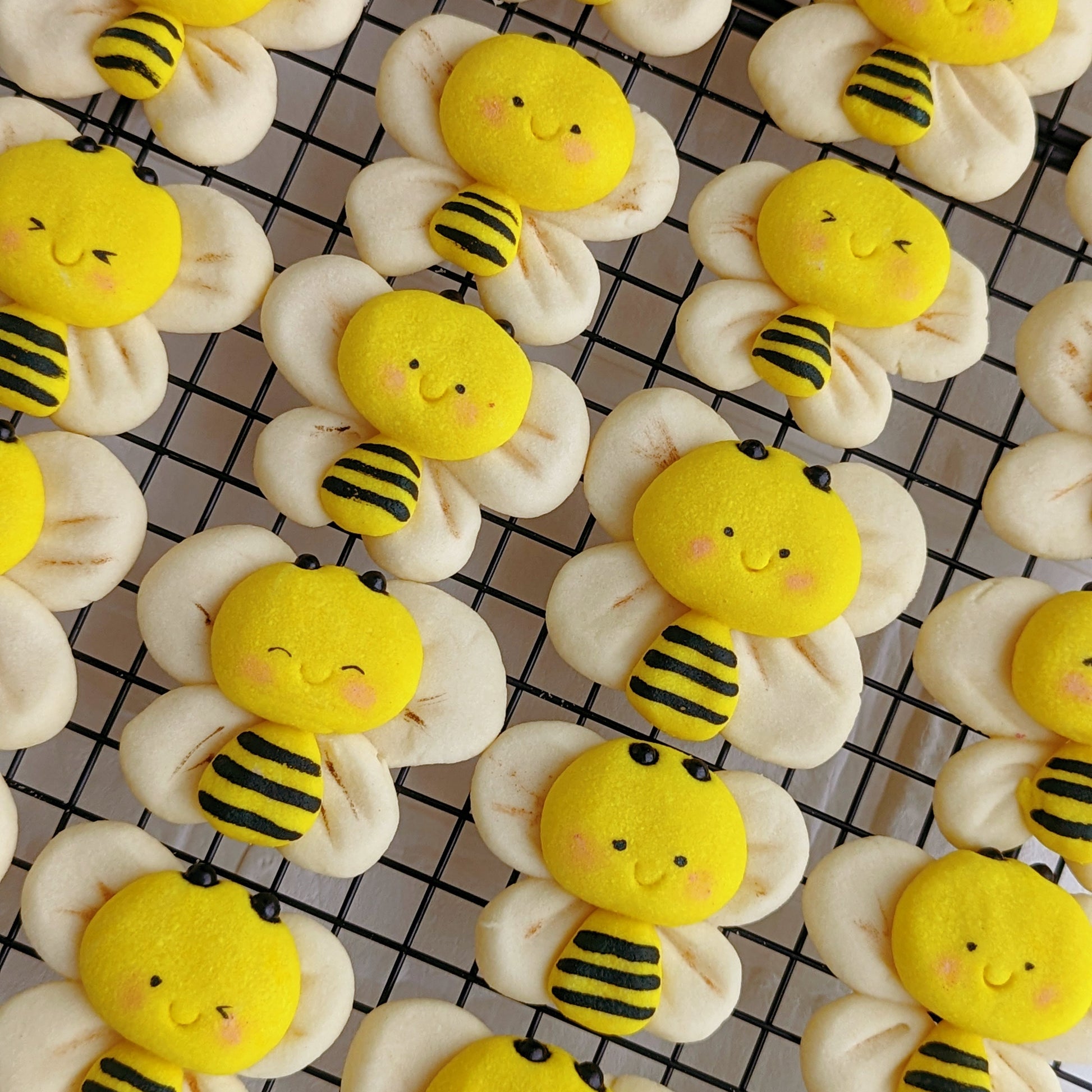 Handmade 3D bumble bee-shaped shortbread cookies on a cooling rack — yellow and black striped bee body with cream-coloured wing cookies, rosy cheeks, and a smiling face. Made to order by The Good Cupcakes, Singapore.
