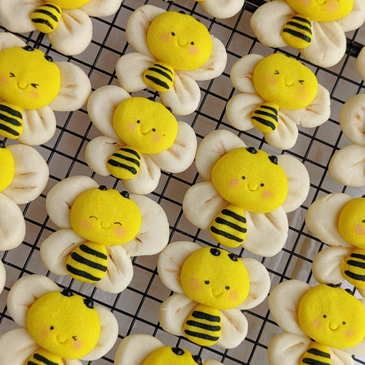 Handmade 3D bumble bee-shaped shortbread cookies on a cooling rack — yellow and black striped bee body with cream-coloured wing cookies, rosy cheeks, and a smiling face. Made to order by The Good Cupcakes, Singapore.
