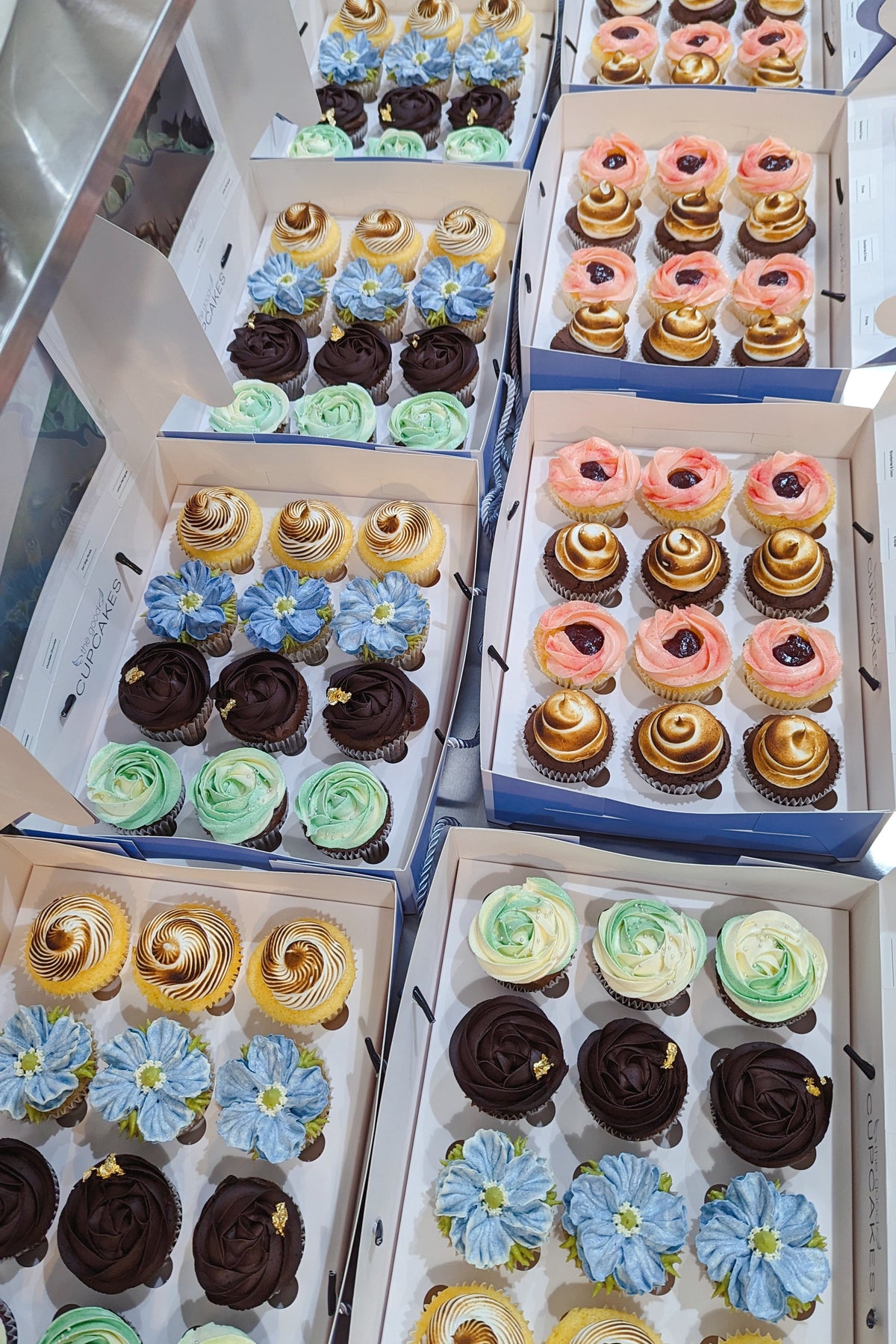 Multiple open boxes of assorted floral, chocolate, berry and toasted-meringue cupcakes prepared for MINDEF Singapore.