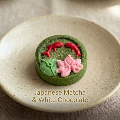 Japanese Matcha & White Chocolate shortbread cookie with hand-piped koi fish and lotus leaf design, on a speckled ceramic plate.