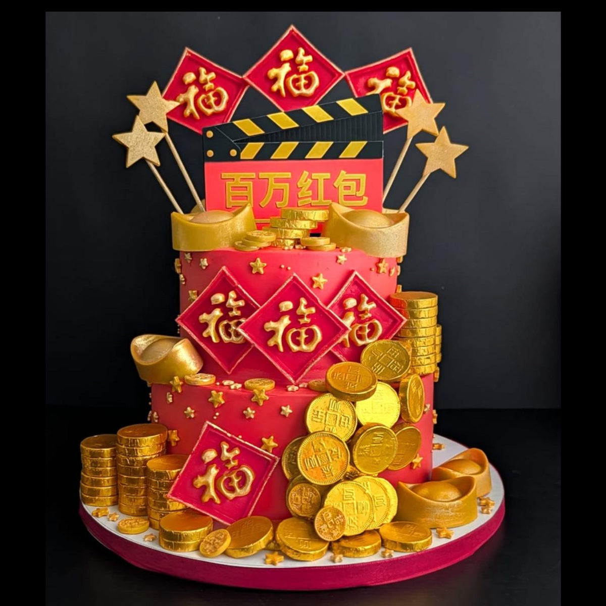 Red two-tier cake made for a movie premiere, decorated with a clapperboard, lucky red packets and gold coins.