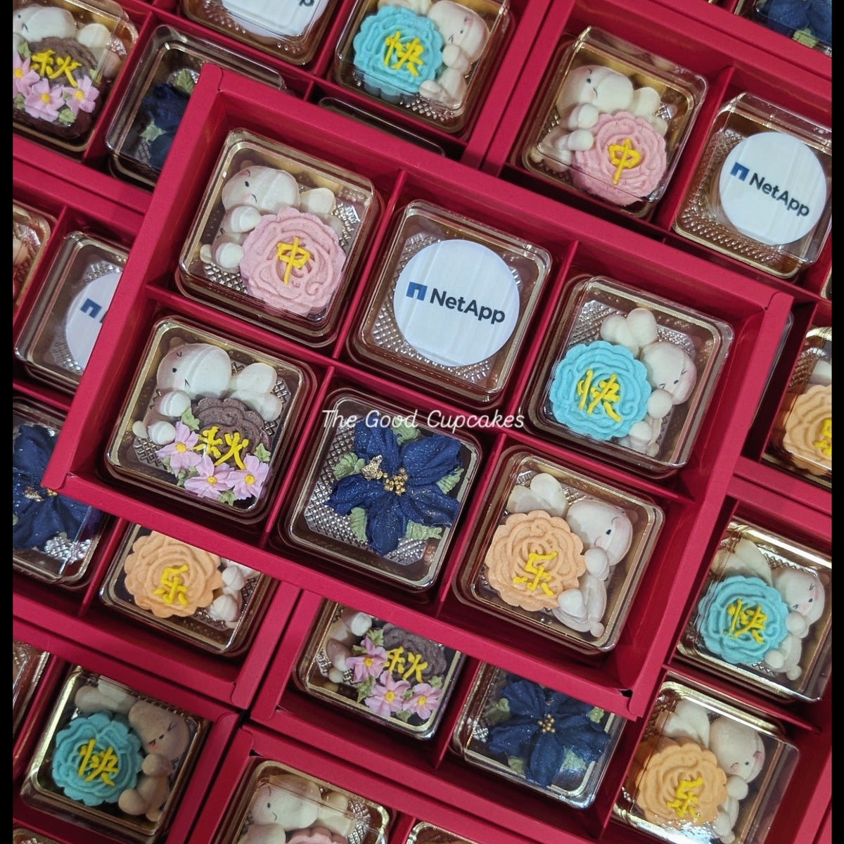 Red Mid-Autumn gift boxes filled with decorated cupcakes featuring NetApp logo toppers, flowers, rabbits and Chinese characters.