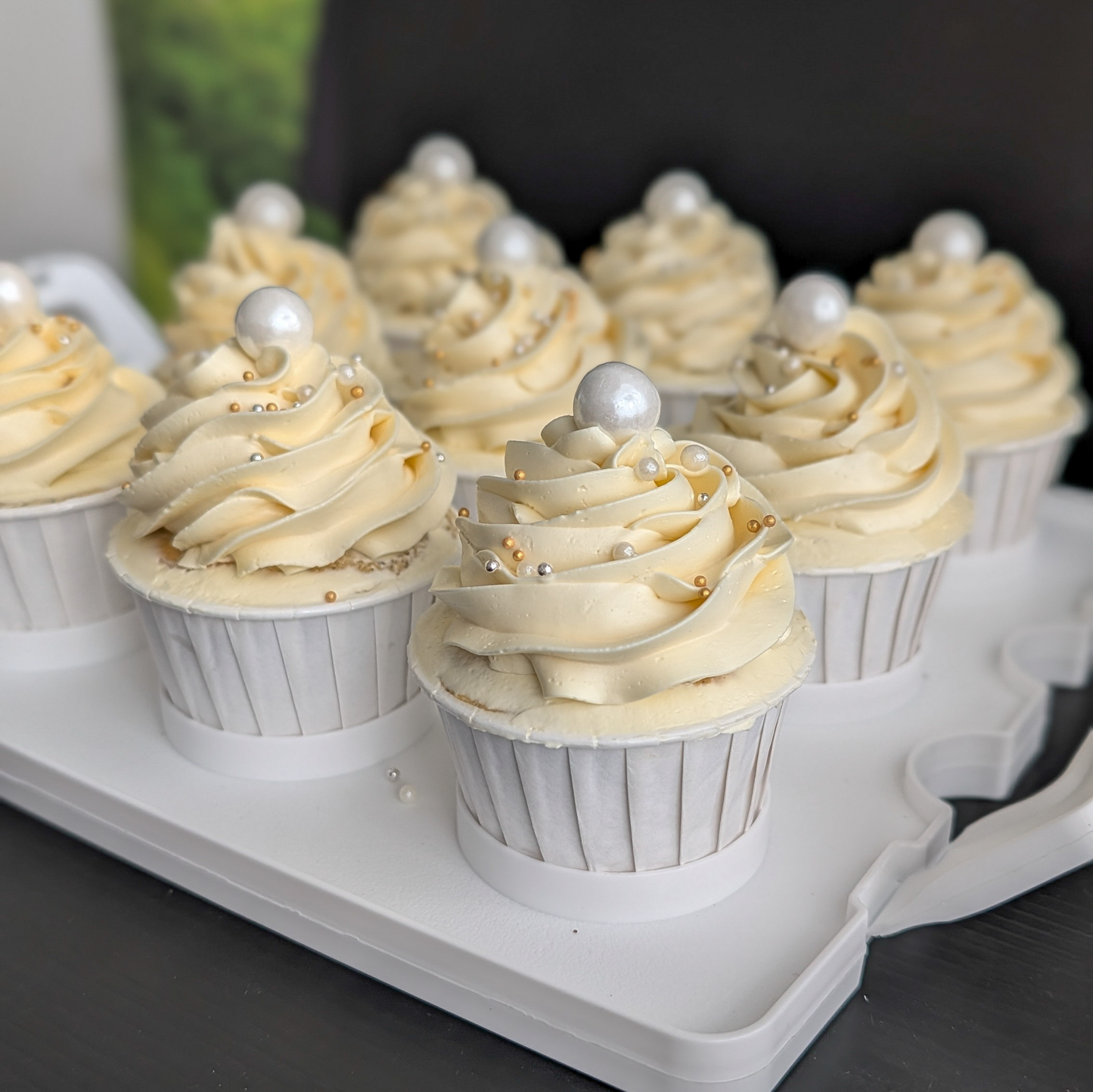 Cupcakes on a white tray—  ivory buttercream swirls topped with a white pearl and gold and silver dragees