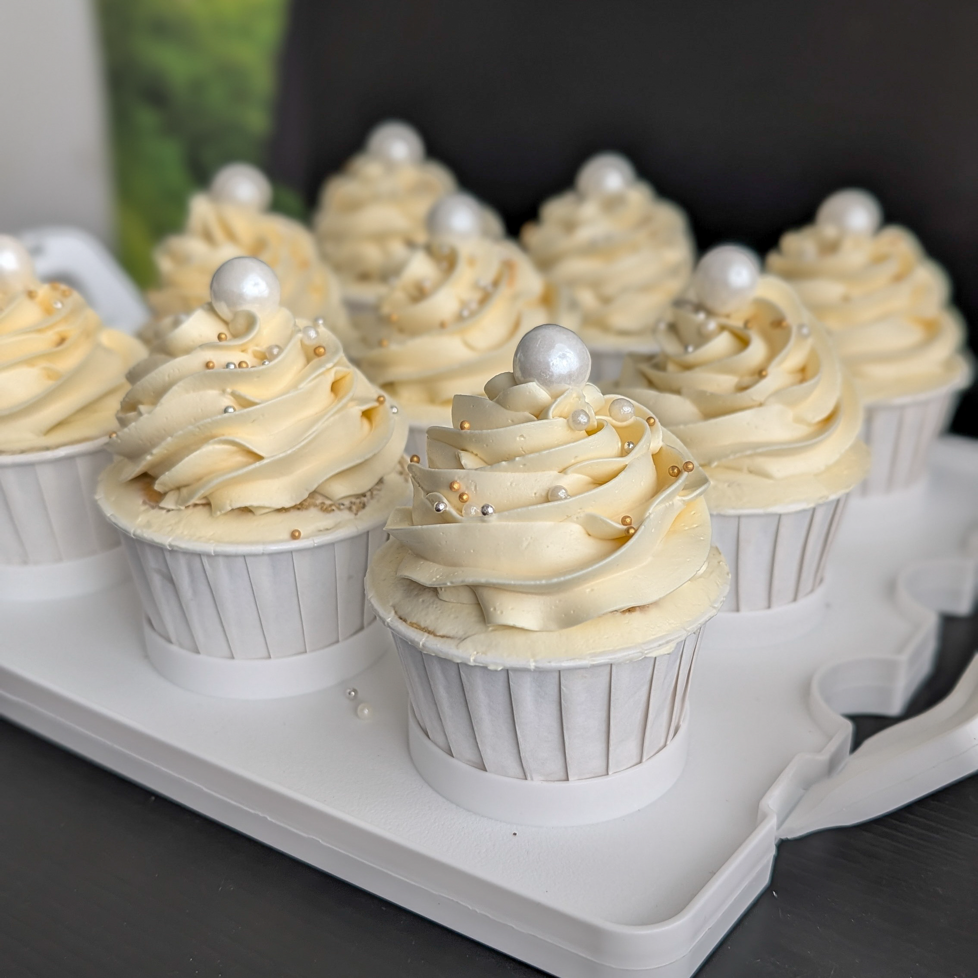 Cupcakes on a white tray—  ivory buttercream swirls topped with a white pearl and gold and silver dragees