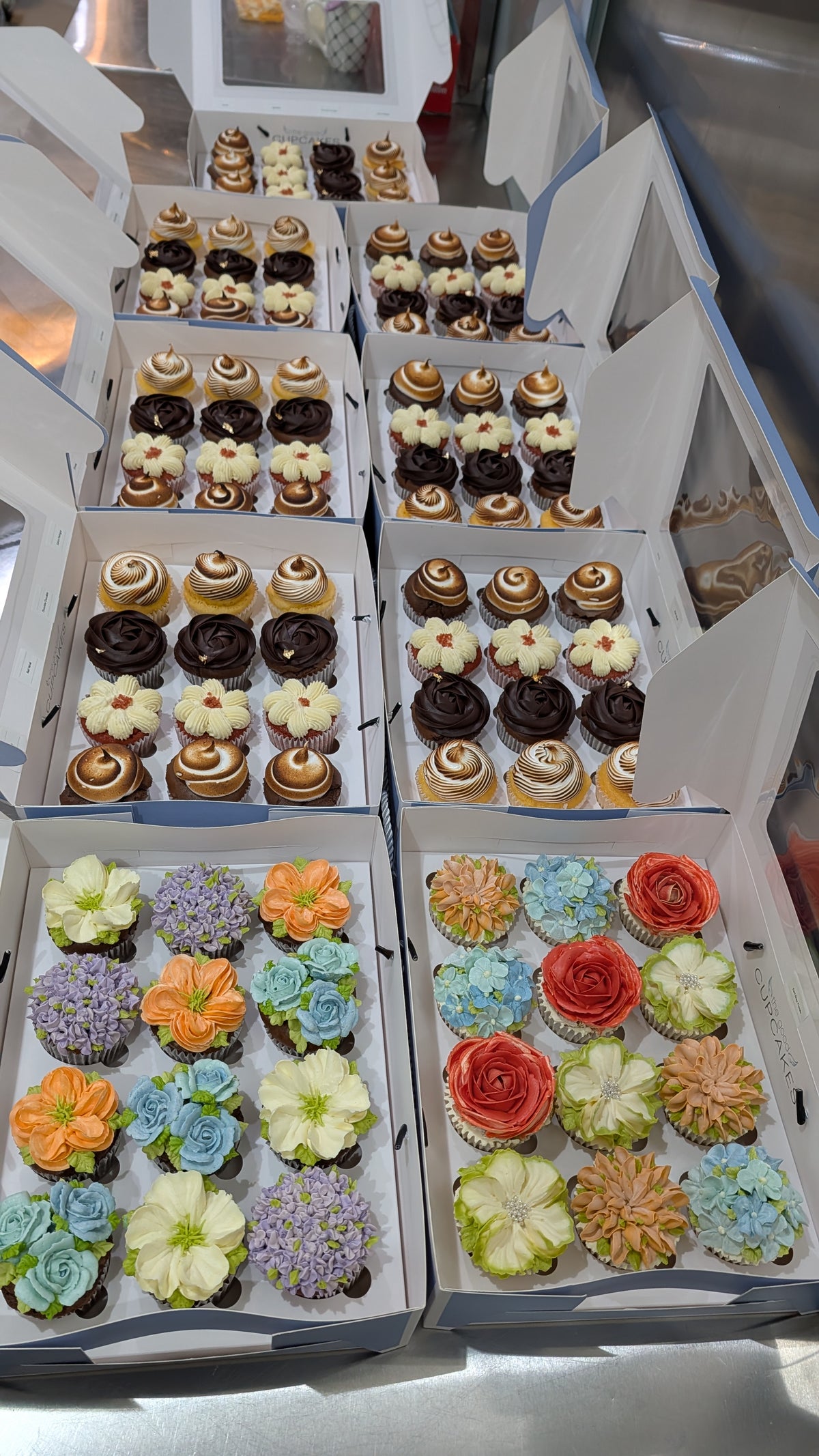 Multiple open boxes of assorted cupcakes featuring toasted meringue, chocolate swirls and hand-piped floral designs for a Standard Chartered seminar.