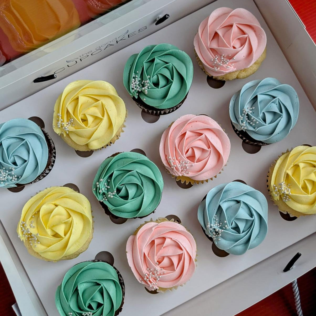 Box of 12 chocolate cupcakes with pastel rose-piped buttercream in pink, blue, green and yellow with silver pearl sprinkles, The Good Cupcakes Singapore
