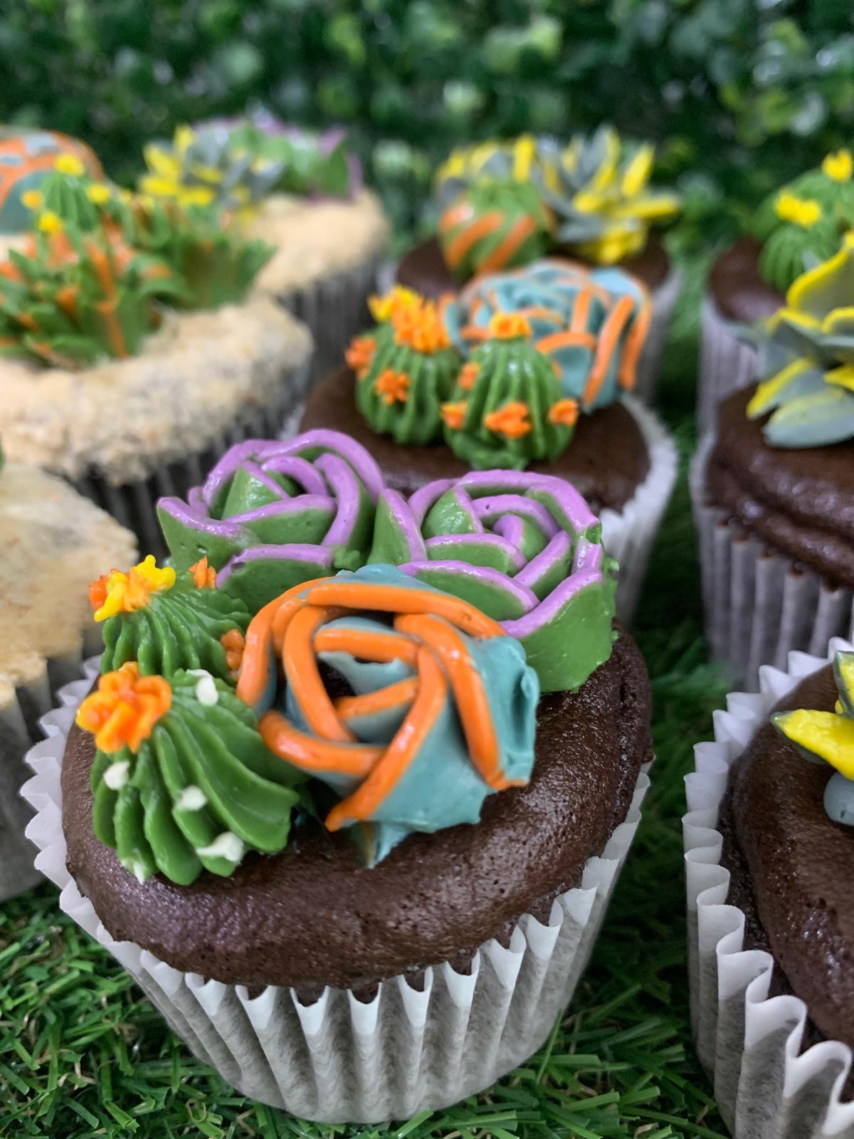 Diagonal row of succulent cupcakes on grass display, purple and orange piped buttercream succulents — The Good Cupcakes Singapore