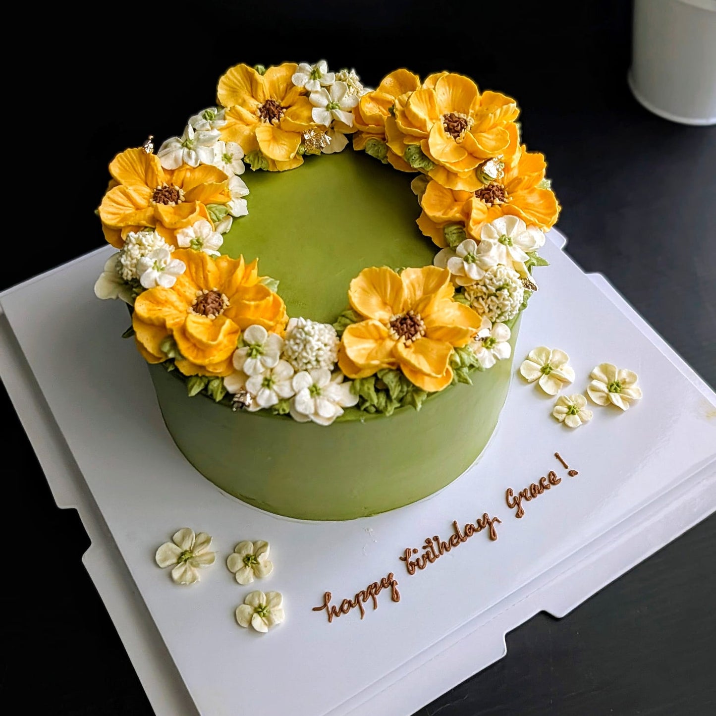 Matcha green birthday cake with hand-piped yellow sunflower and white blossom buttercream wreath, floral wreath cake Singapore