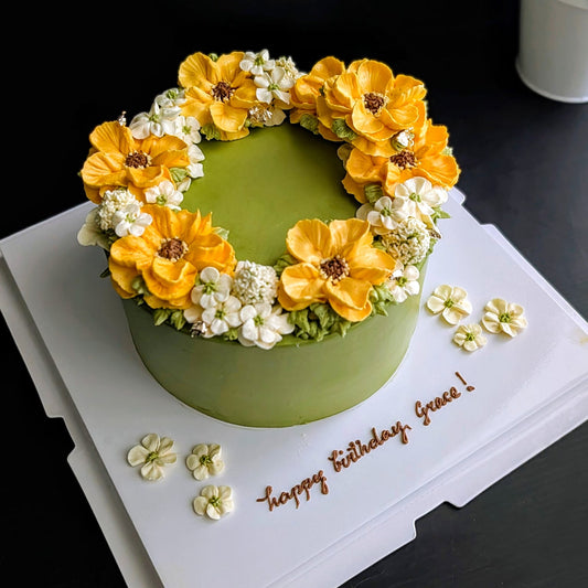 Matcha green birthday cake with hand-piped yellow sunflower and white blossom buttercream wreath, floral wreath cake Singapore