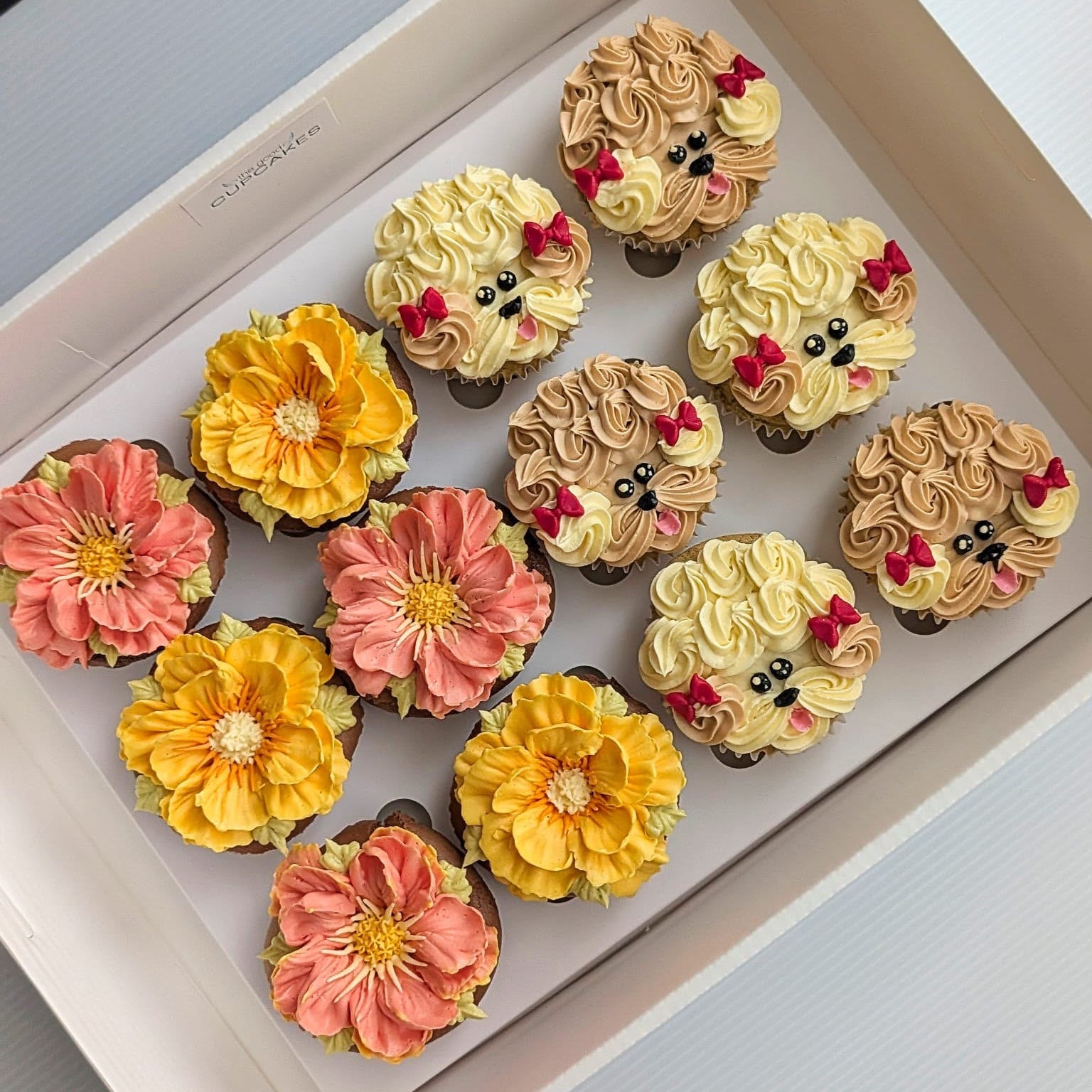 Box of 12 cupcakes with 6 hand-piped puppy face cupcakes in white, brown and grey buttercream and 6 hand-piped floral cupcakes in pink and yellow, The Good Cupcakes Singapore