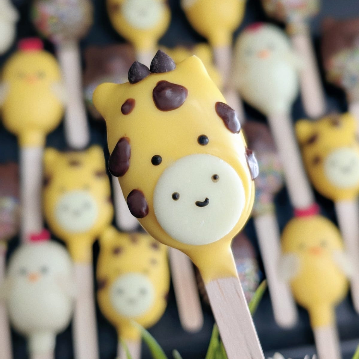 Giraffe cakesicle - yellow with brown spots, surrounded by animal friends