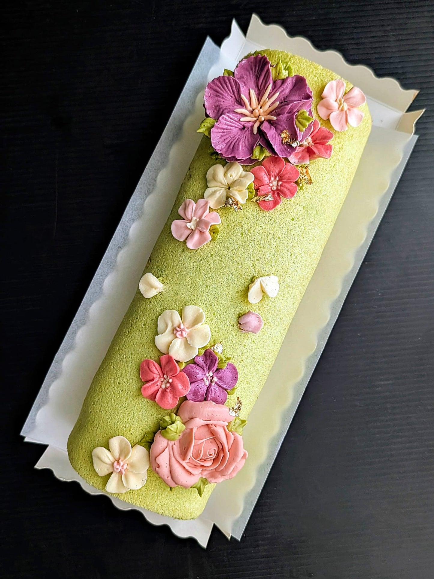 low sugar Swiss roll cake with piped buttercream floral topper featuring purple hibiscus, pink roses, coral and white blossoms, elegant roll cake Singapore