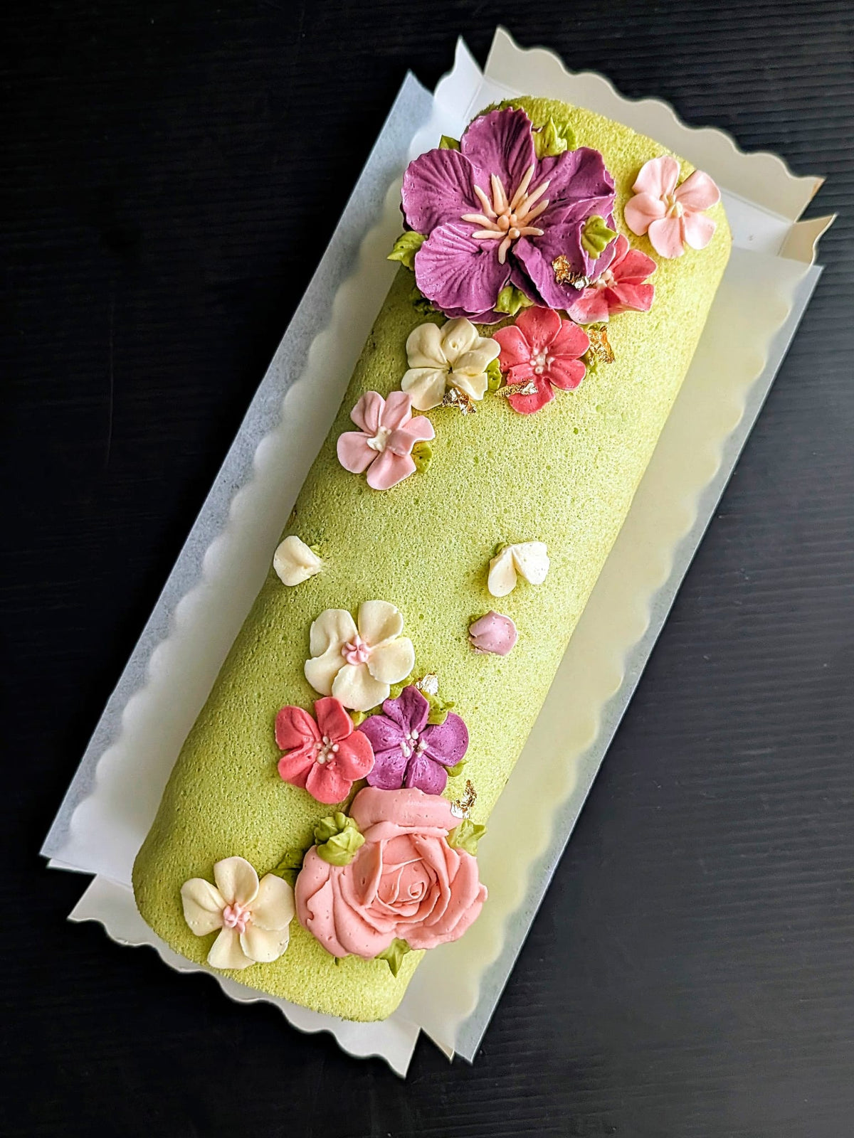 low sugar Swiss roll cake with piped buttercream floral topper featuring purple hibiscus, pink roses, coral and white blossoms, elegant roll cake Singapore