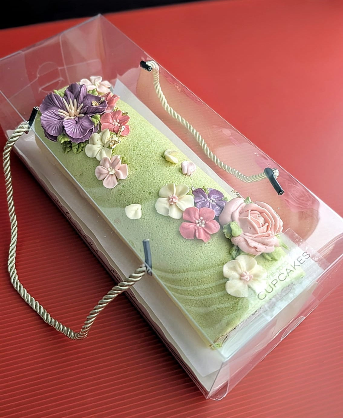 low sugar Swiss roll cake with piped buttercream floral topper featuring purple hibiscus, pink roses, coral and white blossoms, elegant roll cake Singapore