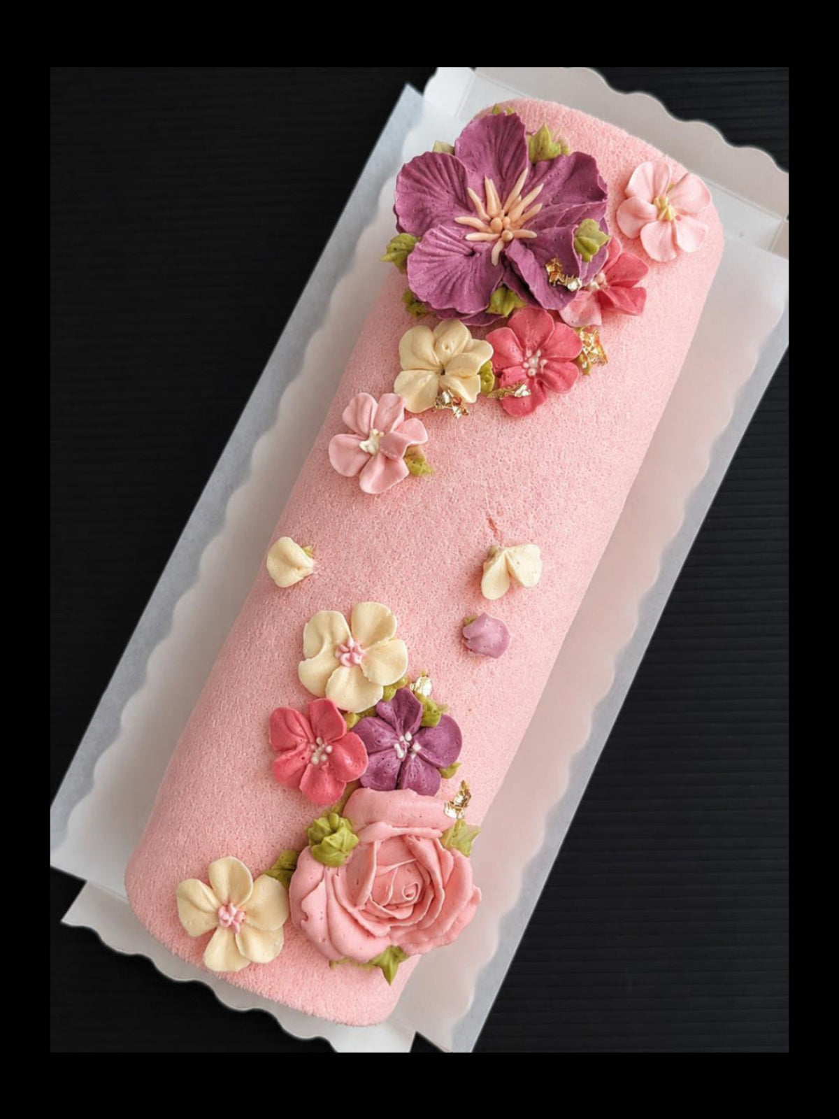 low sugar Swiss roll cake with piped buttercream floral topper featuring purple hibiscus, pink roses, coral and white blossoms, elegant roll cake Singapore