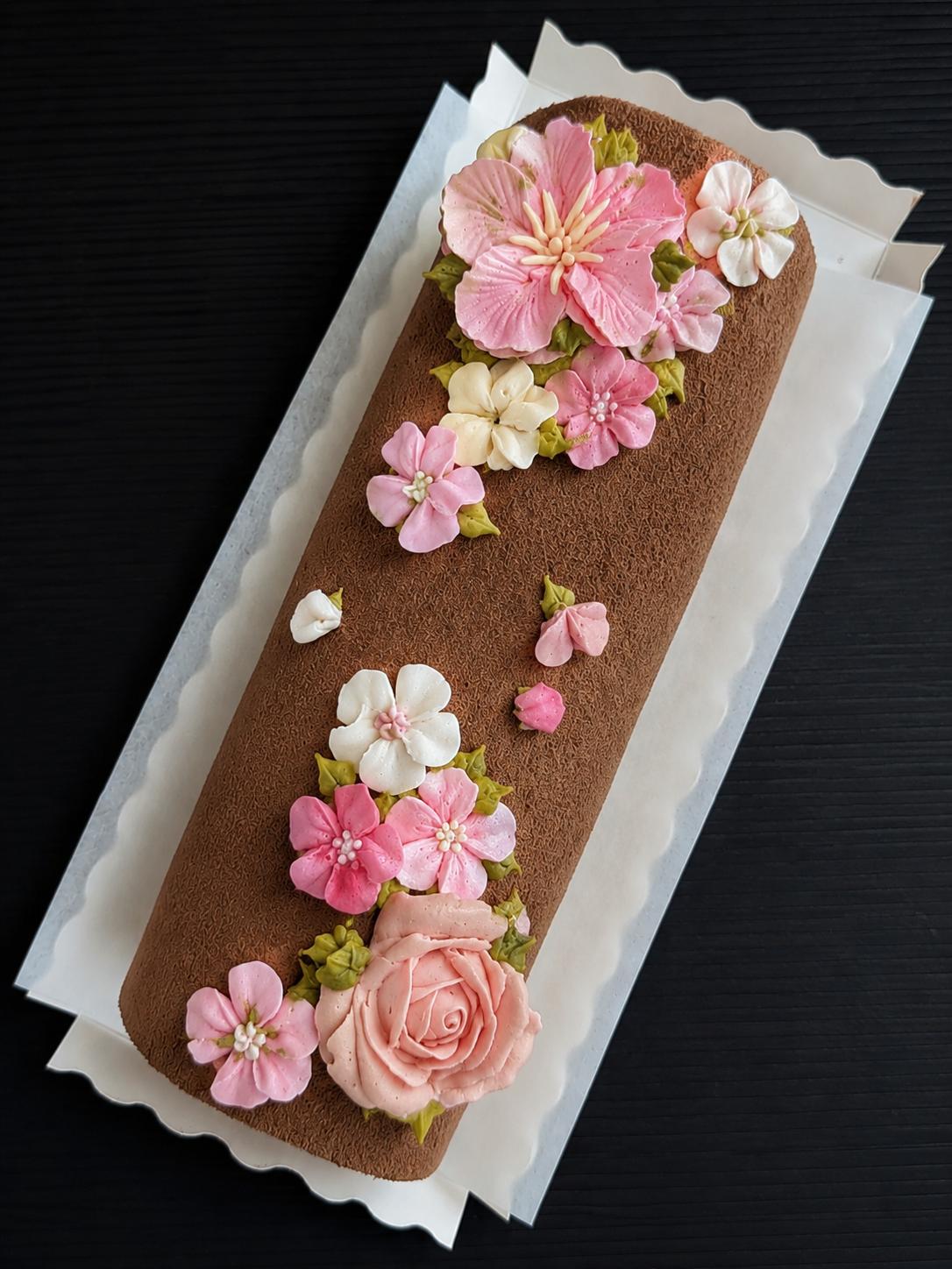 low sugar Swiss roll cake with piped buttercream floral topper featuring purple hibiscus, pink roses, coral and white blossoms, elegant roll cake Singapore