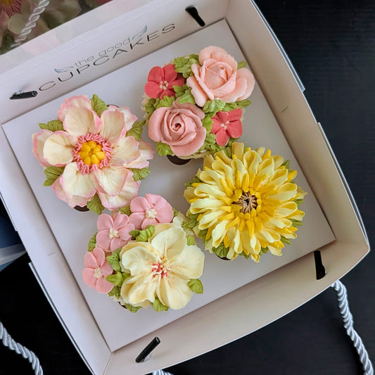 Four handcrafted floral buttercream cupcakes in a The Good Cupcakes gift box — featuring a peony, rose, chrysanthemum and magnolia in pink, yellow and cream