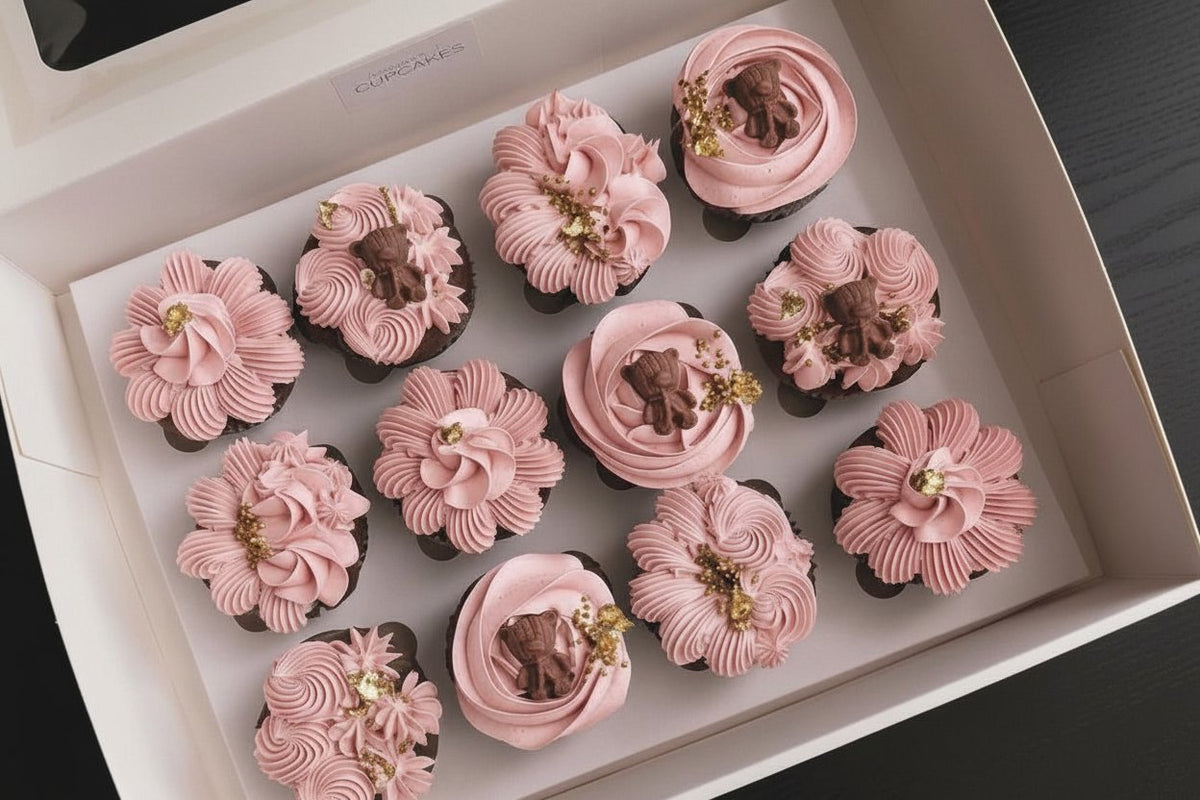 Box of 12 gender reveal cupcakes with hand-piped pink buttercream florals, teddy bear toppers and gold leaf, The Good Cupcakes Singapore
