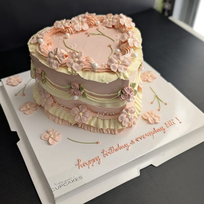 Heart-shaped vintage cake with blush pink buttercream ruffles, piped floral details and pearl accents, romantic low-sugar birthday cake Singapore