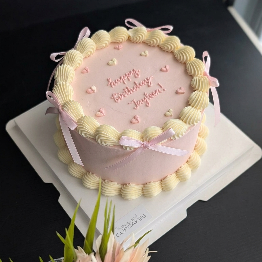 Pink vintage birthday cake with cream buttercream rosette border, ribbon bows, heart sprinkles and custom piped message, low-sugar celebration cake Singapore